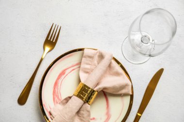 Katlanmış peçeteli tabak, altın çatal bıçak takımı ve grunge beyaz arka planda cam.