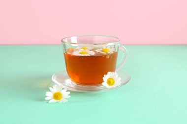 Pembe duvarın yanındaki turkuaz masada bir fincan doğal papatya çayı ve çiçekler.