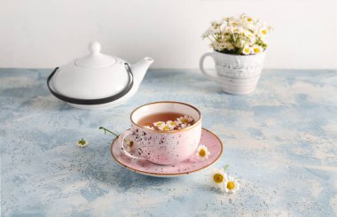 Bir fincan doğal papatya çayıyla çaydanlık ve mavi grunge masasında çiçekler duvarın yanında.