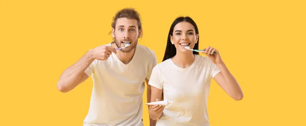 Young couple brushing teeth on yellow background