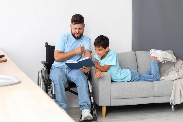 車椅子の父は家で息子に本を読んで — ストック写真