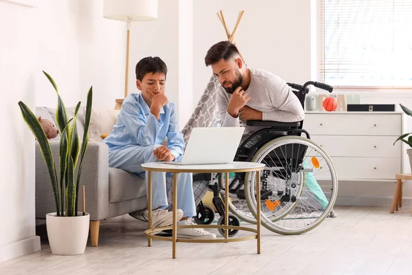 Przemyślany Chłopiec Jego Ojciec Wózku Inwalidzkim Korzystający Laptopa Domu — Zdjęcie stockowe