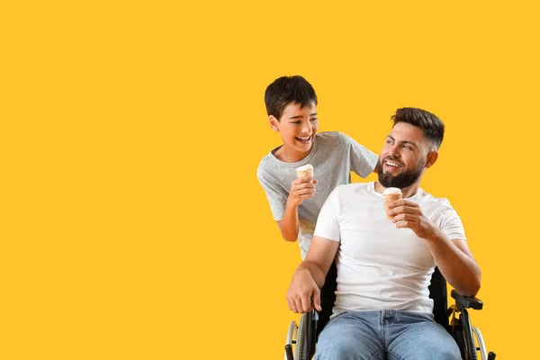 黄色の背景にアイスクリームと車椅子の男の子と彼の父 — ストック写真