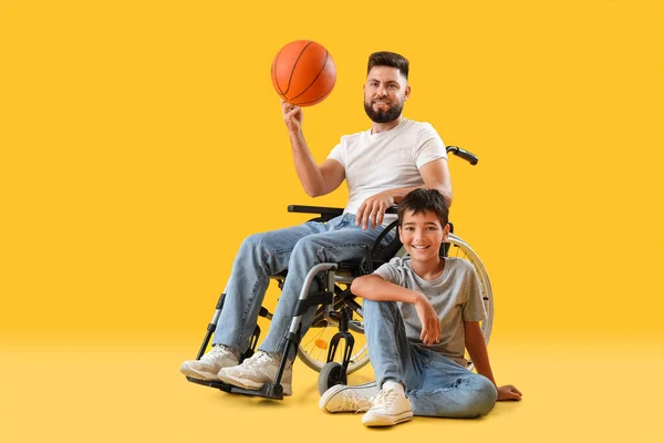 黄色の背景のボールを持つ車椅子の男の子と彼の父親 — ストック写真