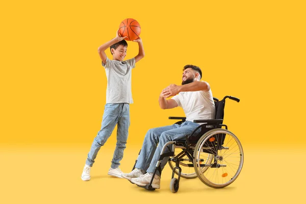 黄色の背景でボールで遊んでいる車椅子の男の子と彼の父親 — ストック写真