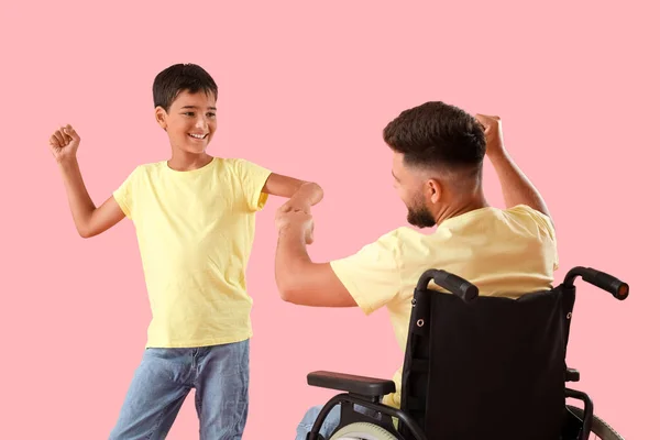 ピンクの背景に車椅子の拳で男の子と彼の父 — ストック写真