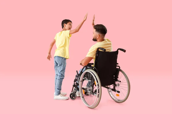 ピンクの背景にお互いを与え合う車椅子の男の子と彼の父親 — ストック写真