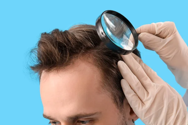 Büyüteçle Doktor Mavi Arka Planda Genç Adamın Saçını Inceliyor — Stok fotoğraf