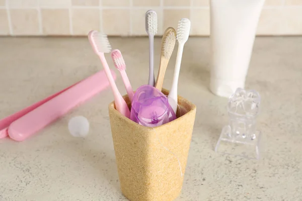 Dental floss in toothbrush holder on table near tile wall