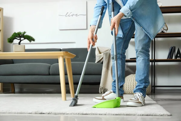 年轻人在家里用扫帚擦地毯 — 图库照片