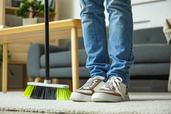 Young man sweeping carpet with broom at home, closeup