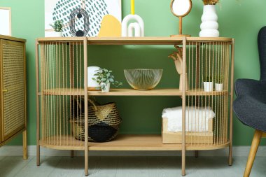 Odadaki yeşil duvarın yanında boyalı ve dekorlu raf ünitesi.