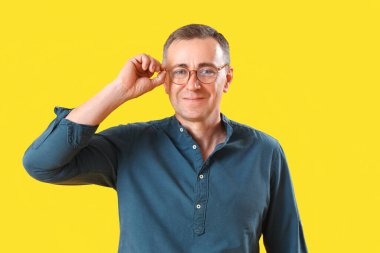 Sarı arka planda gözlüklü olgun bir adam.