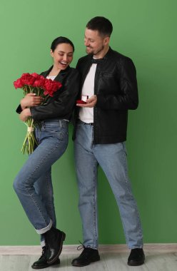 Genç adam yeşil duvarın yanında kız arkadaşına evlenme teklif ediyor.