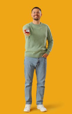 Sarı arka planda nişan yüzüğü olan genç bir adam.