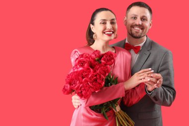 Genç adam kırmızı arka planda kız arkadaşının parmağına nişan yüzüğü takıyor.