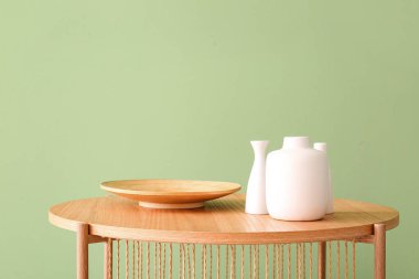 Ahşap sehpa, ahşap tabak ve yeşil duvarın yanında vazolar.