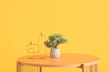 Bonsai ağacıyla ahşap sehpa ve turuncu duvarın yanında dekoratif mum tutacakları.