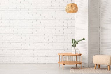 Vazoda okaliptüs dalları olan ahşap sehpa, beyaz tuğla duvarın yanında katlanan ekran ve puf.