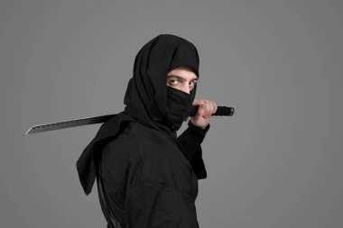Gri arka planda kılıcı olan erkek ninja.