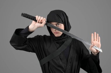 Gri arka planda kılıcı olan erkek ninja.