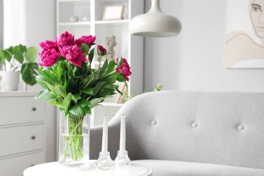 Oturma odasındaki sehpanın üzerinde kırmızı şakayık ve mumlar olan vazo.