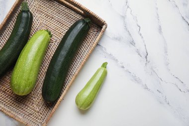 Beyaz mermer zemin üzerinde taze kabak ile hasır tepsi