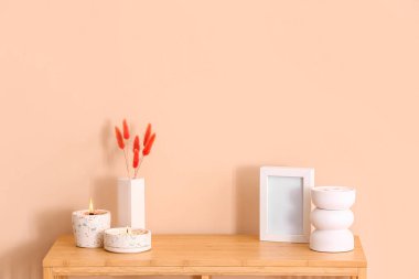 Odadaki bej duvarın yanındaki masada yanan mumlar ve boş çerçeveli tutucular.