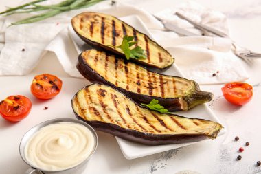 Hafif arka planda ızgara patlıcan, sos ve domates tabağı.