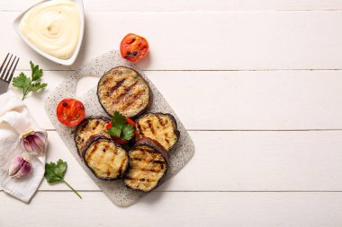 Beyaz ahşap arka planda leziz ızgara patlıcan, sos ve domates.