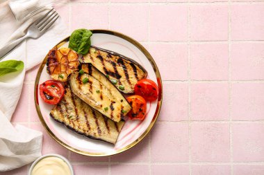 Pembe arka planda lezzetli ızgara patlıcan, domates ve sarımsak tabağı.