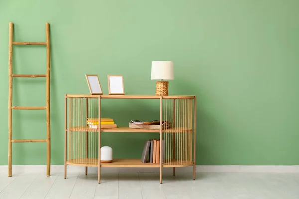 部屋の緑の壁の近くに空白のフレーム ランプ 本やはしごを持つスタイリッシュな木製の棚ユニット — ストック写真