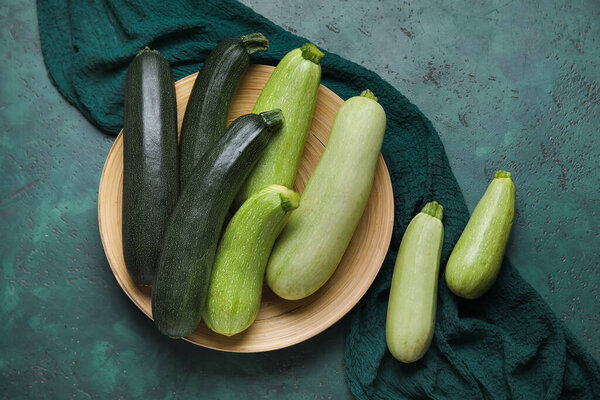 Plate with fresh zucchini on green background