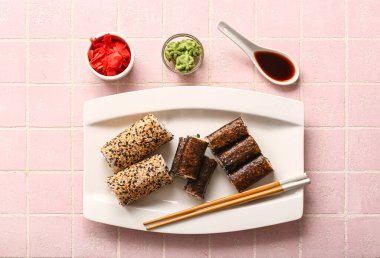 Lezzetli suşi ruloları, zencefil, wasabi ve pembe arkaplanda soya sosu.