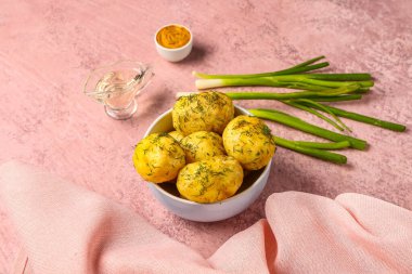 Bir kase haşlanmış patates, pembe arka planda dereotu ve yeşil soğanlı.