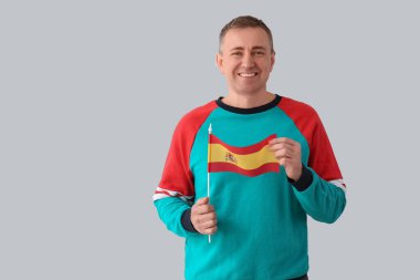 Hafif arka planda İspanya bayrağı taşıyan olgun bir adam.