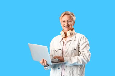 Mavi arka planda dizüstü bilgisayarla çalışan olgun bir kadın programcı.