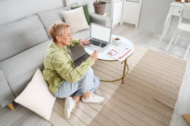 Evde tablet bilgisayar ve dizüstü bilgisayarla çalışan olgun bir kadın programcı