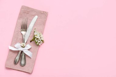 Çiçek açan ağaç dalı ve çatal bıçak takımı pembe arka planda peçeteyle katlanmış.