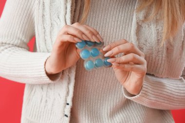 Kırmızı arka planda boğaz ağrısı için hapları olan hasta genç bir kadın.