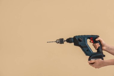 Bej arka planda matkapla dönen çekiç tutan kadın eller.