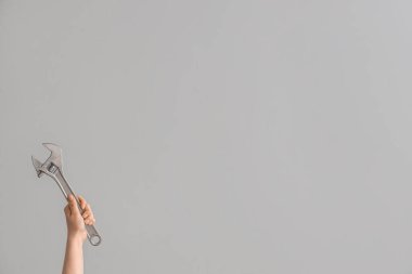 Gri arkaplanda ayarlanabilir İngiliz anahtarı tutan kadın.