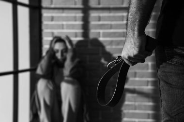 Kemeri olan genç bir adam ve evde korkmuş karısı, yakın plan. Aile içi şiddet kavramı