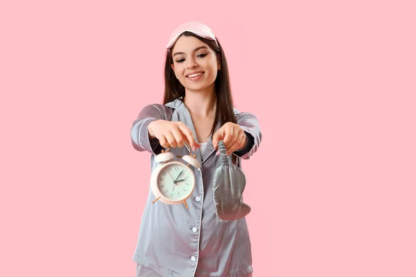 若いです女性でパジャマで目覚まし時計と睡眠マスク上のピンクの背景 — ストック写真