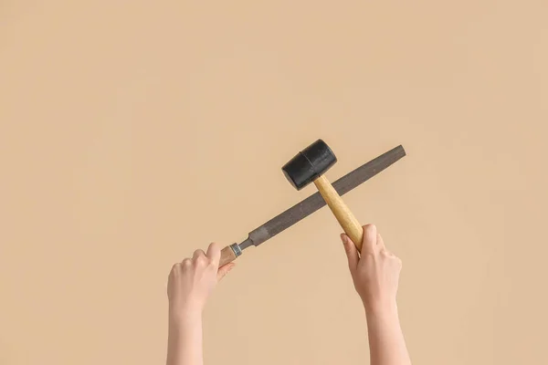 Female hands holding rubber mallet and rasp on beige background