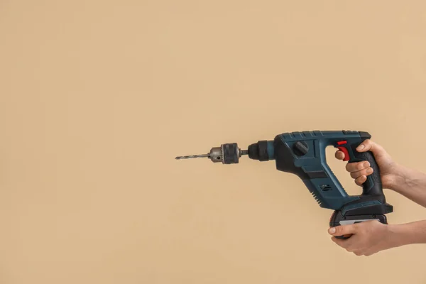 Female hands holding rotary hammer with drill on beige background