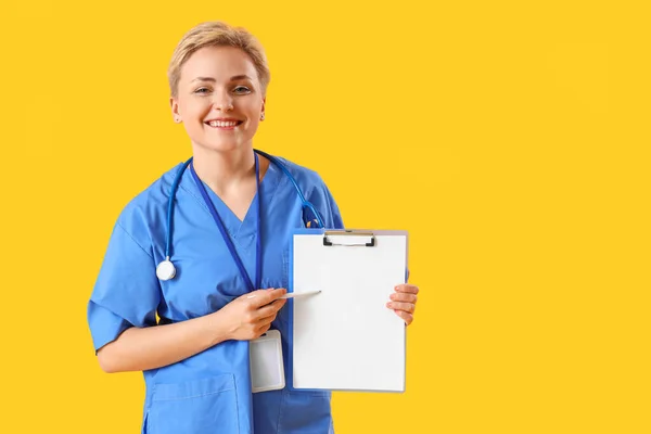 Female Medical Intern Pointing Clipboard Yellow Background — Stock Photo, Image