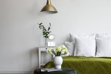 Işıl ışıl yatak odasının içinde rahat bir yatak odası ve pouf üzerinde narsis çiçekleri.