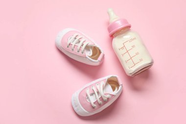 Soluk pembe arka planda kalçalı bebek için bir şişe süt.