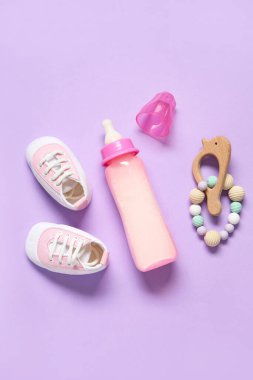 Bebek için bir şişe süt, çıngıraklı ve kalçaları leylak arkaplanlı